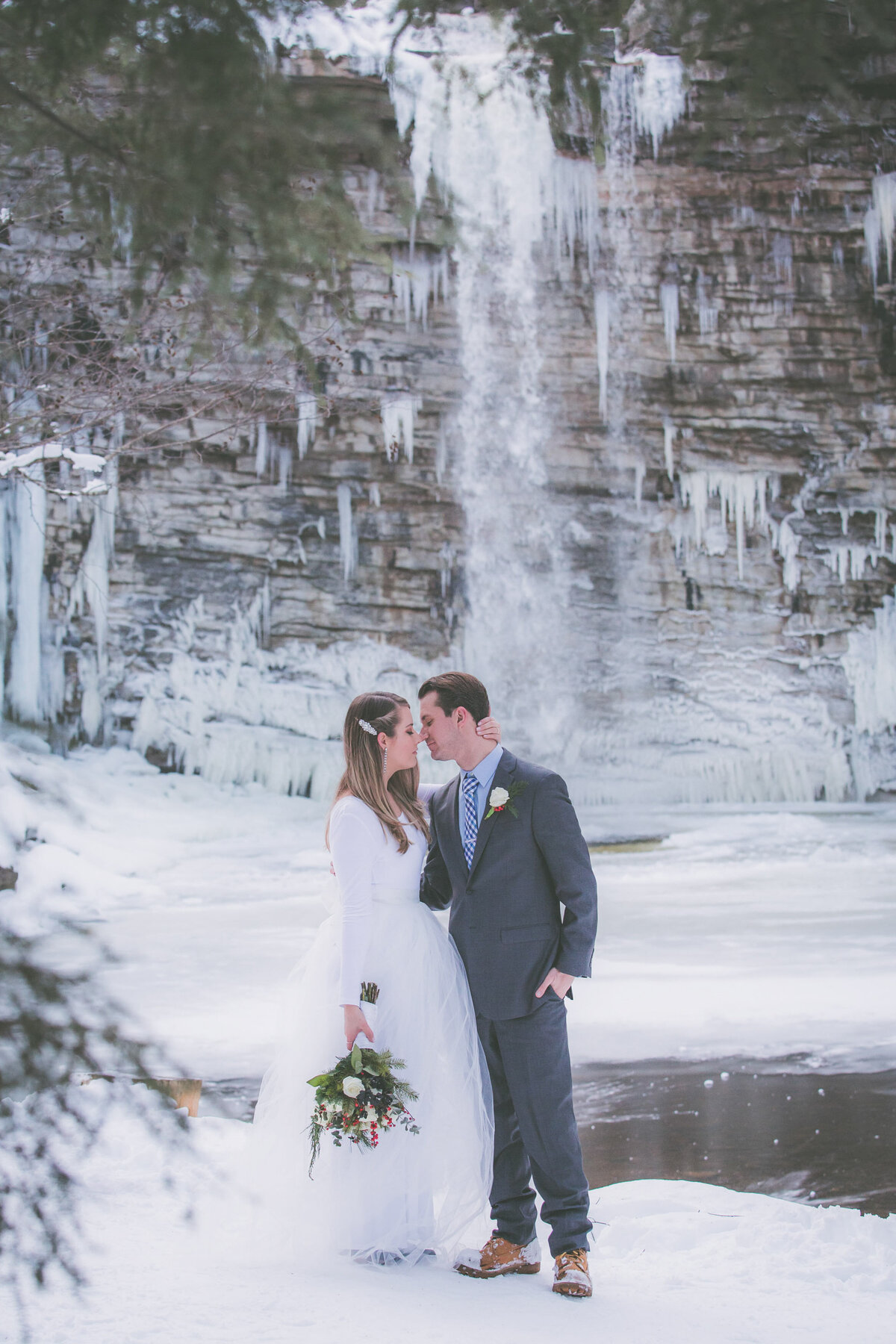 Couple almost kisses with frozen waterfall in background.
