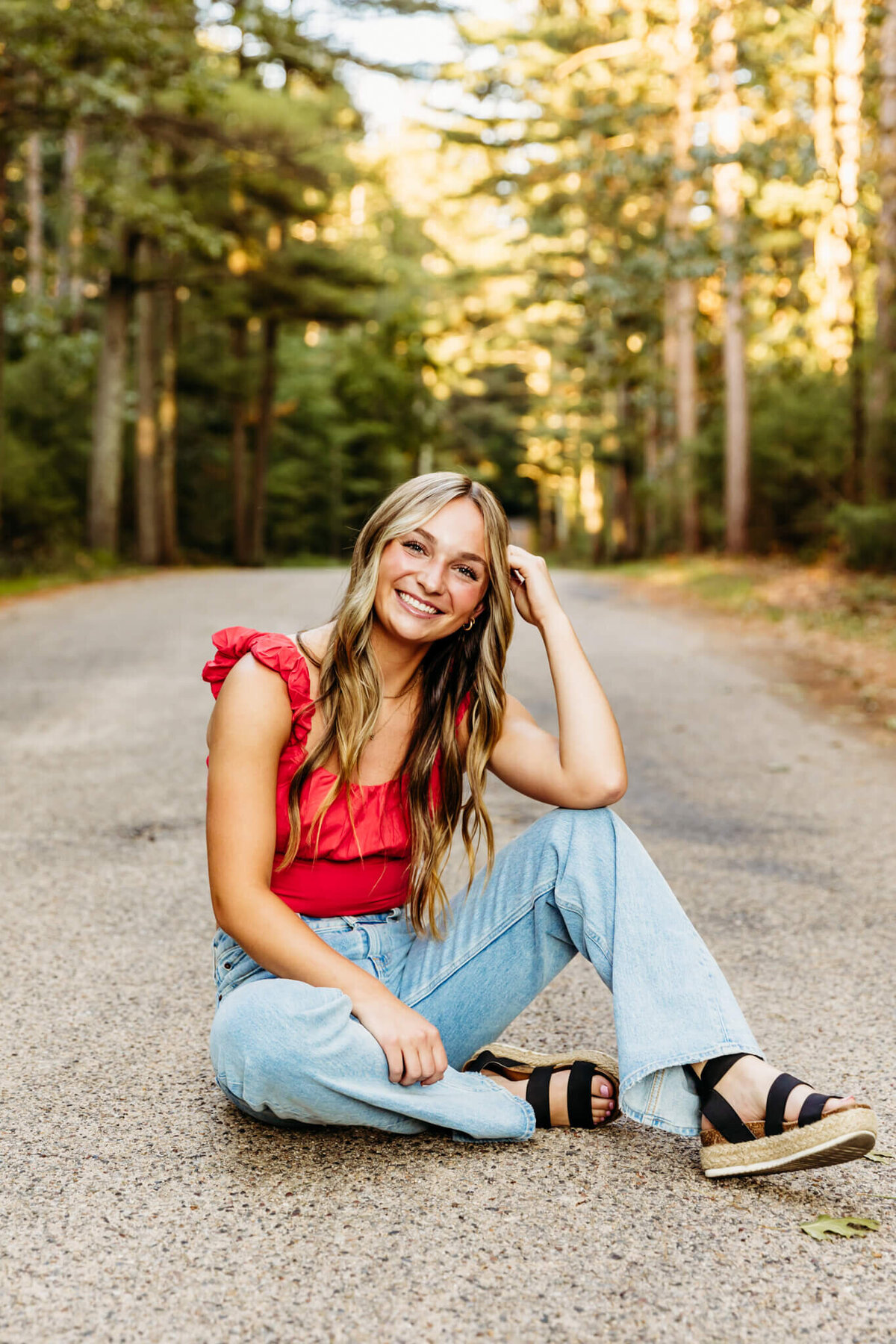 teen girl in a red crop top sitting on a back road while resting her elbow on her knee and leaning against her hand