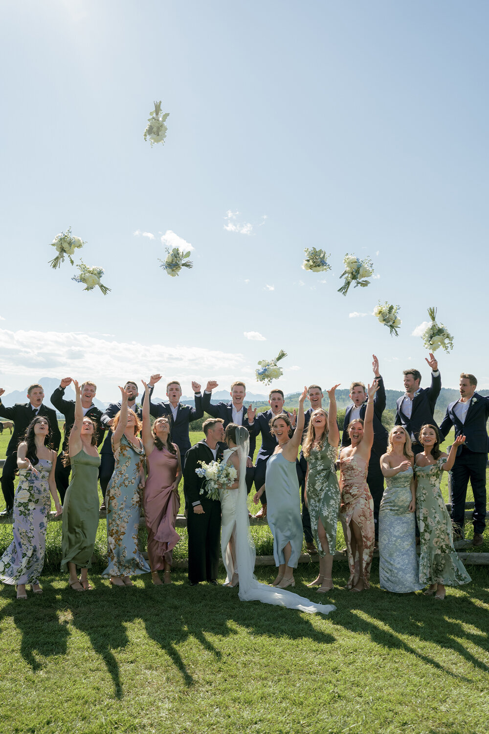 Wedding party celebrating as they cheer and toss their bouquets into the air, framing the bride and groom in a romantic kiss during a summer wedding in Jackson, WY.
