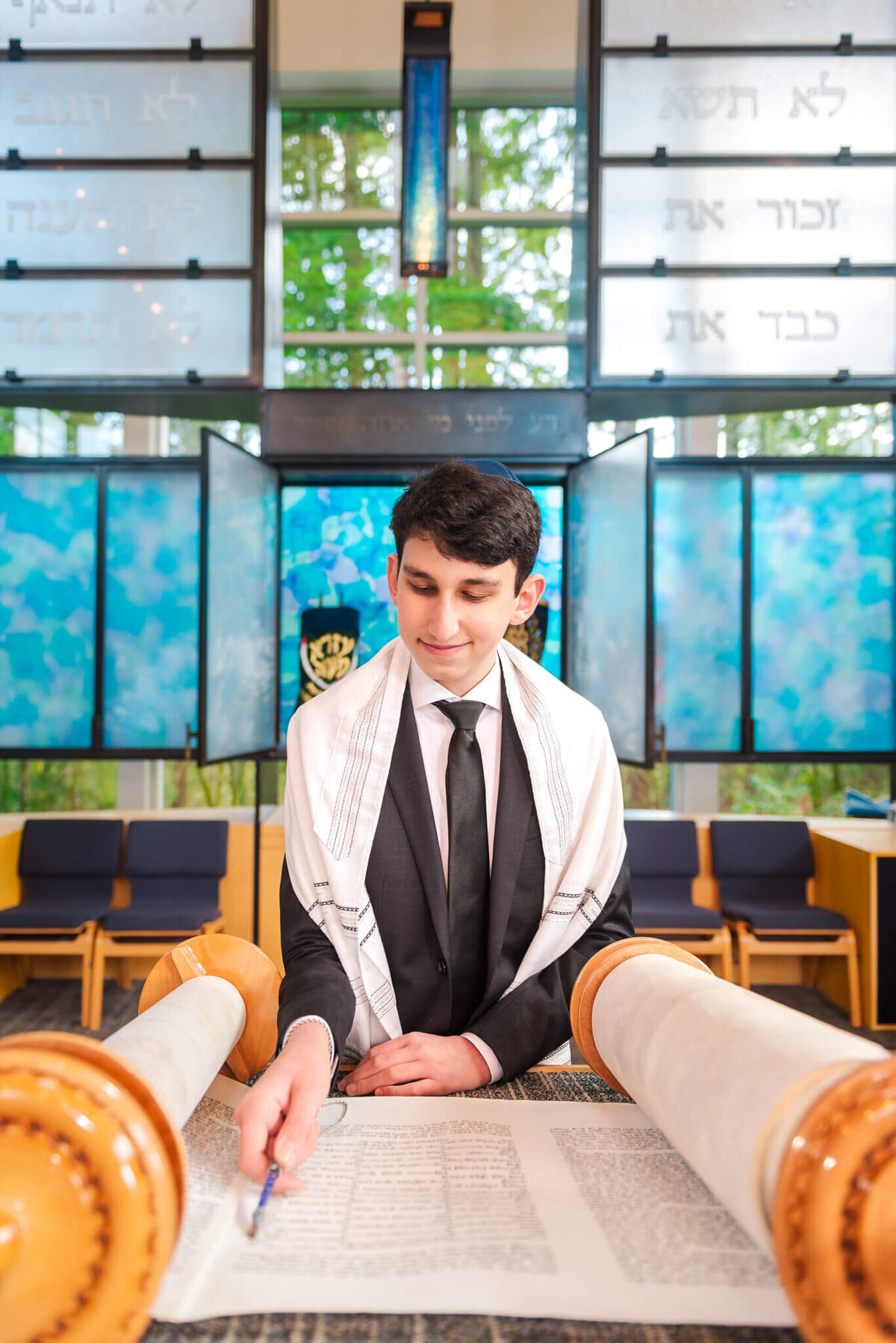 A teenage boy reads from the torah at the bimah in his tallit with a smile for some Bellevue Bar and Bat Mitzvah Photography
