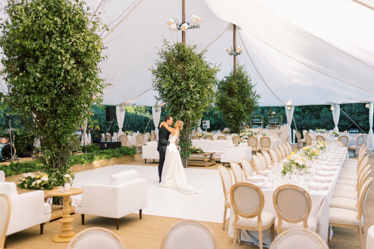 Bride and groom dance in an empty tented wedding reception space to pose for a wedding photo