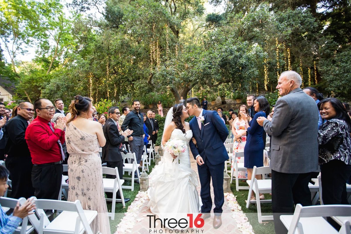 Newly married couple share a kiss at the end of the aisle