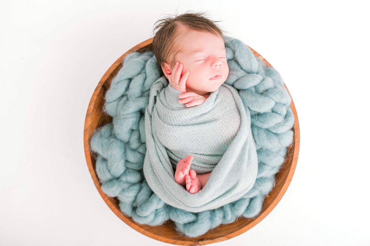 Newborn boy in a bowl with blue blankets and wraps
