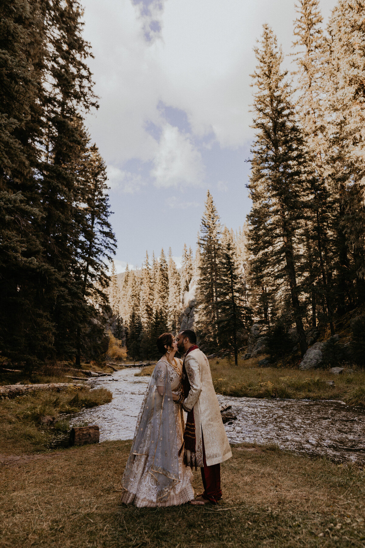bride and groom in Indian attire holding each other in front of a creek in NM