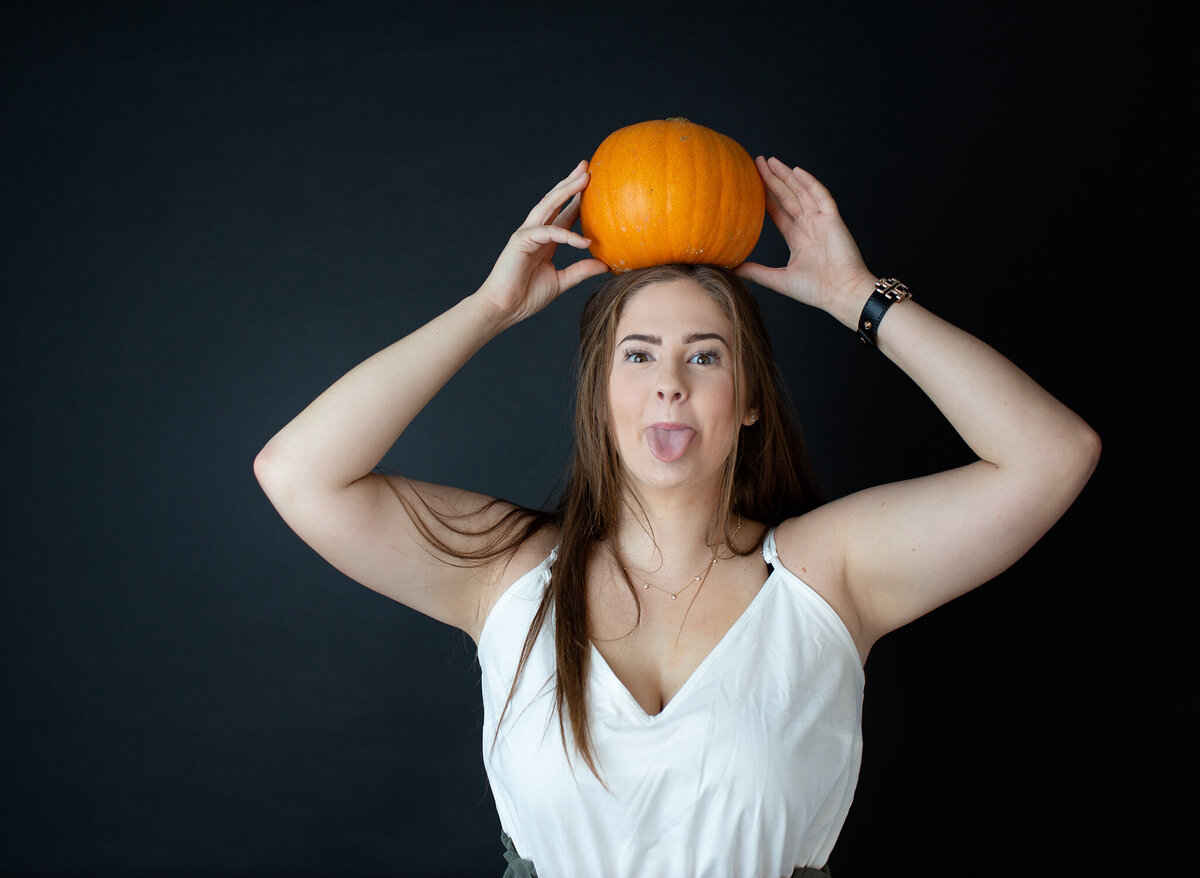 Studio senior girl creative session with pumpkin on head and tongue out