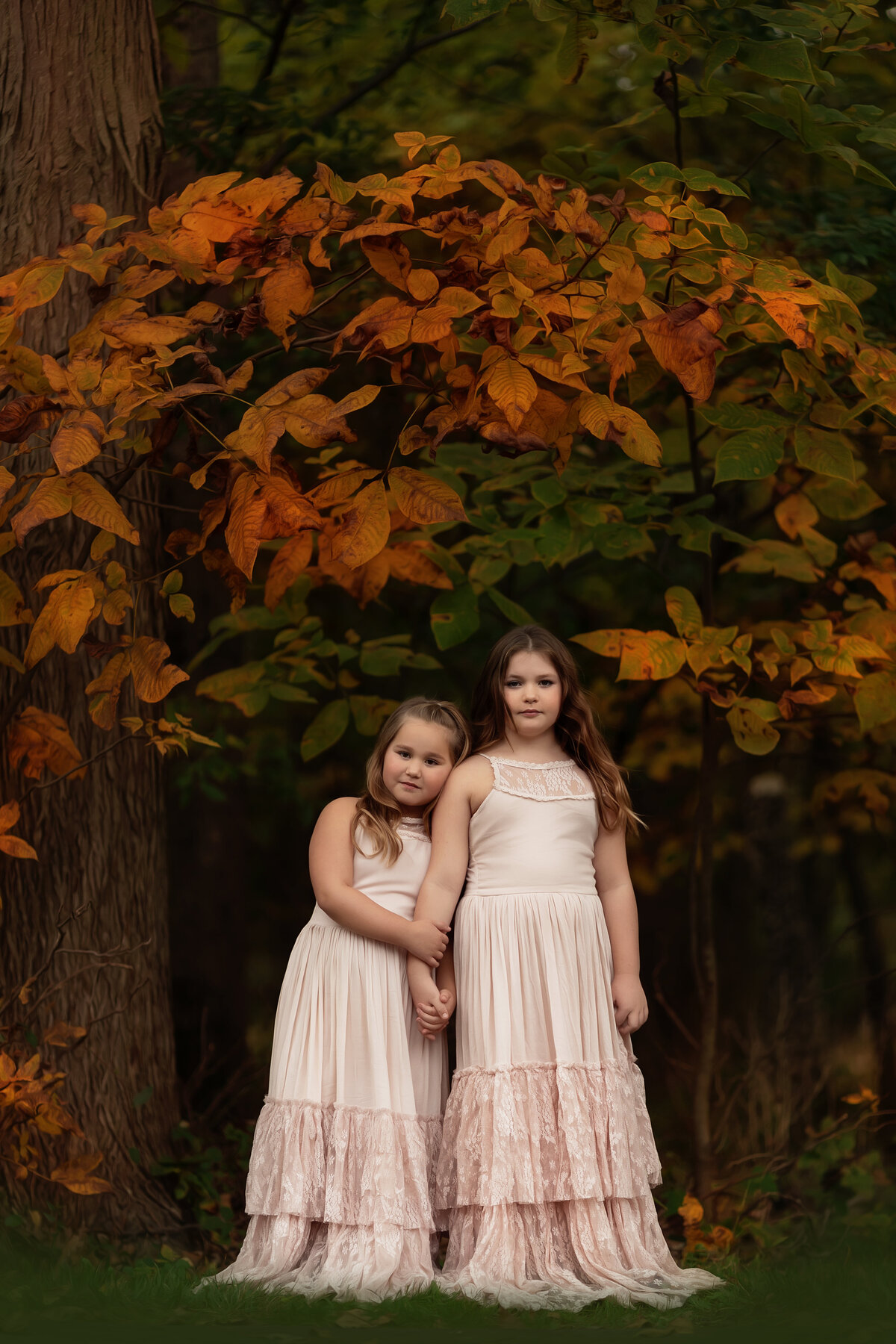 Two sisters in matching long pink dresses hold hands while standing in a forest lawn taken by a New Jersey Family Photographer