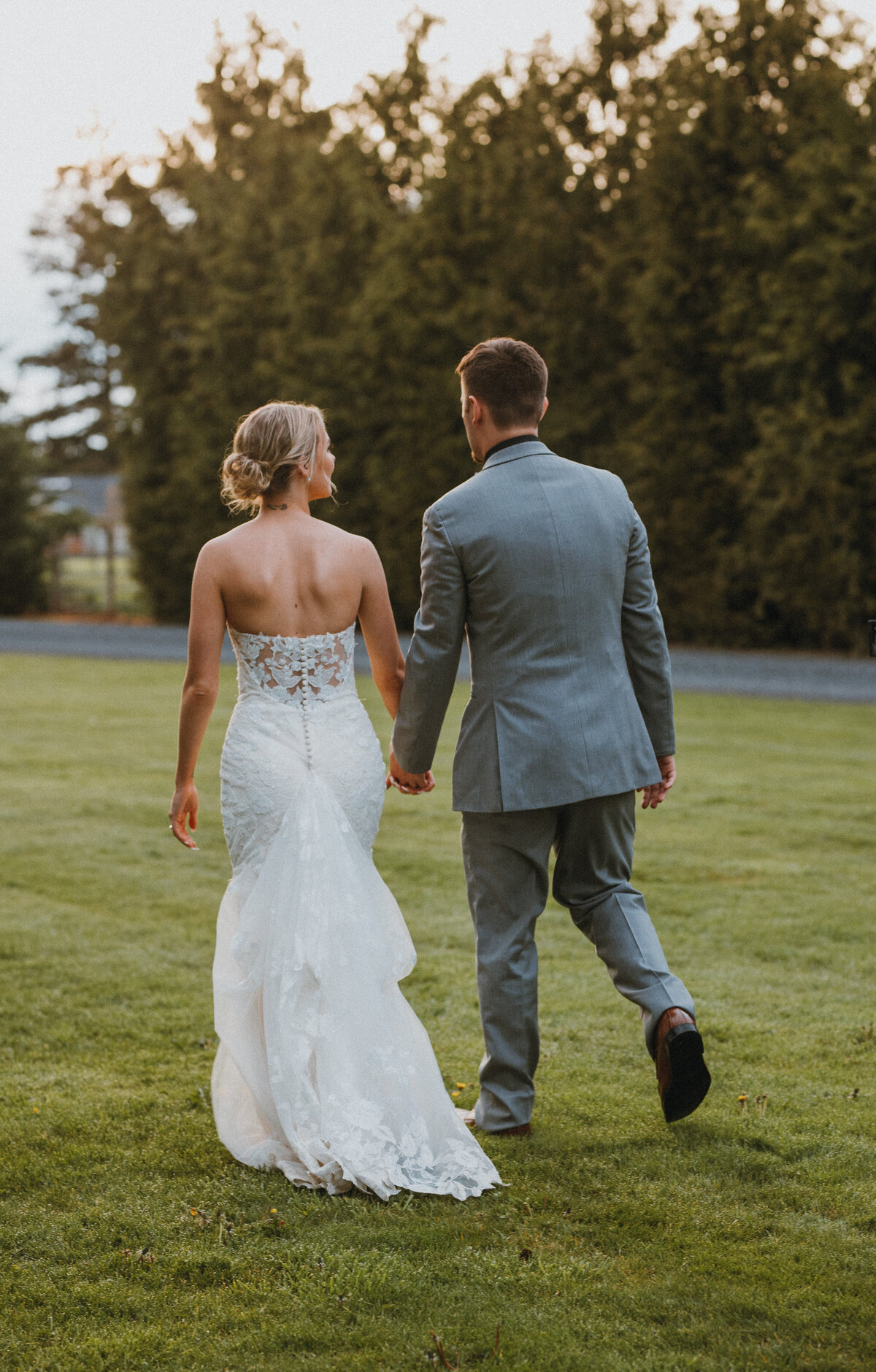 Bride and groom holding hands walking on a green lawn