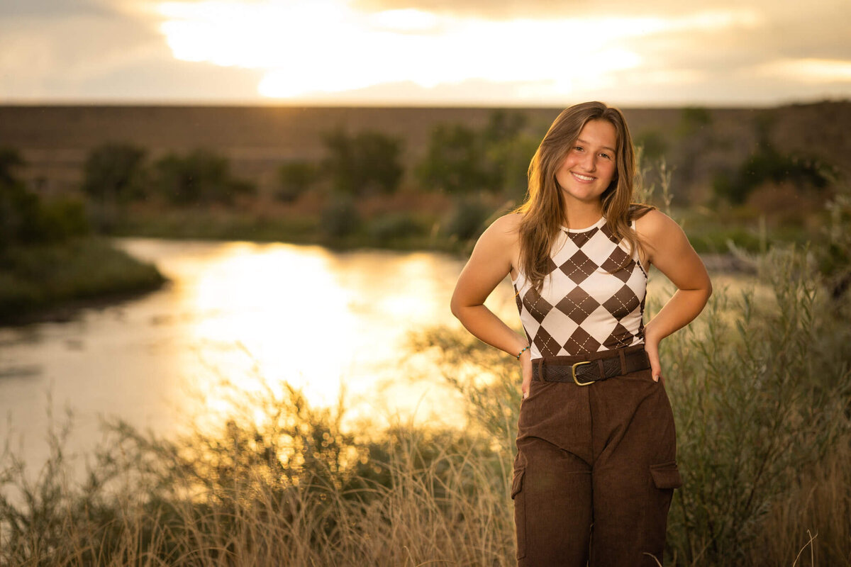high school senior girl standing in front of of a river at sunset