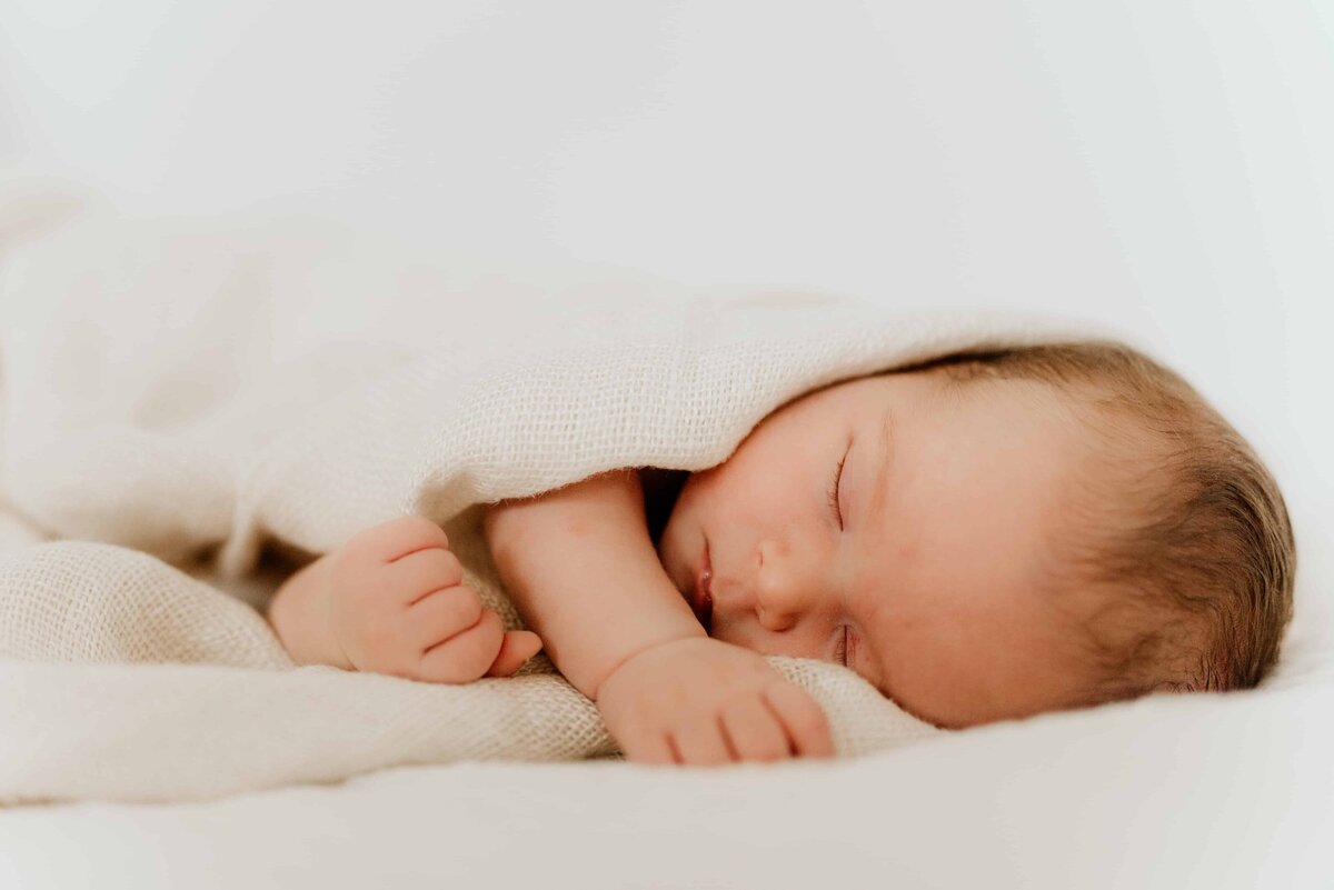 En nyfødt jente ligger på siden og sover under nyfødtfotografering.