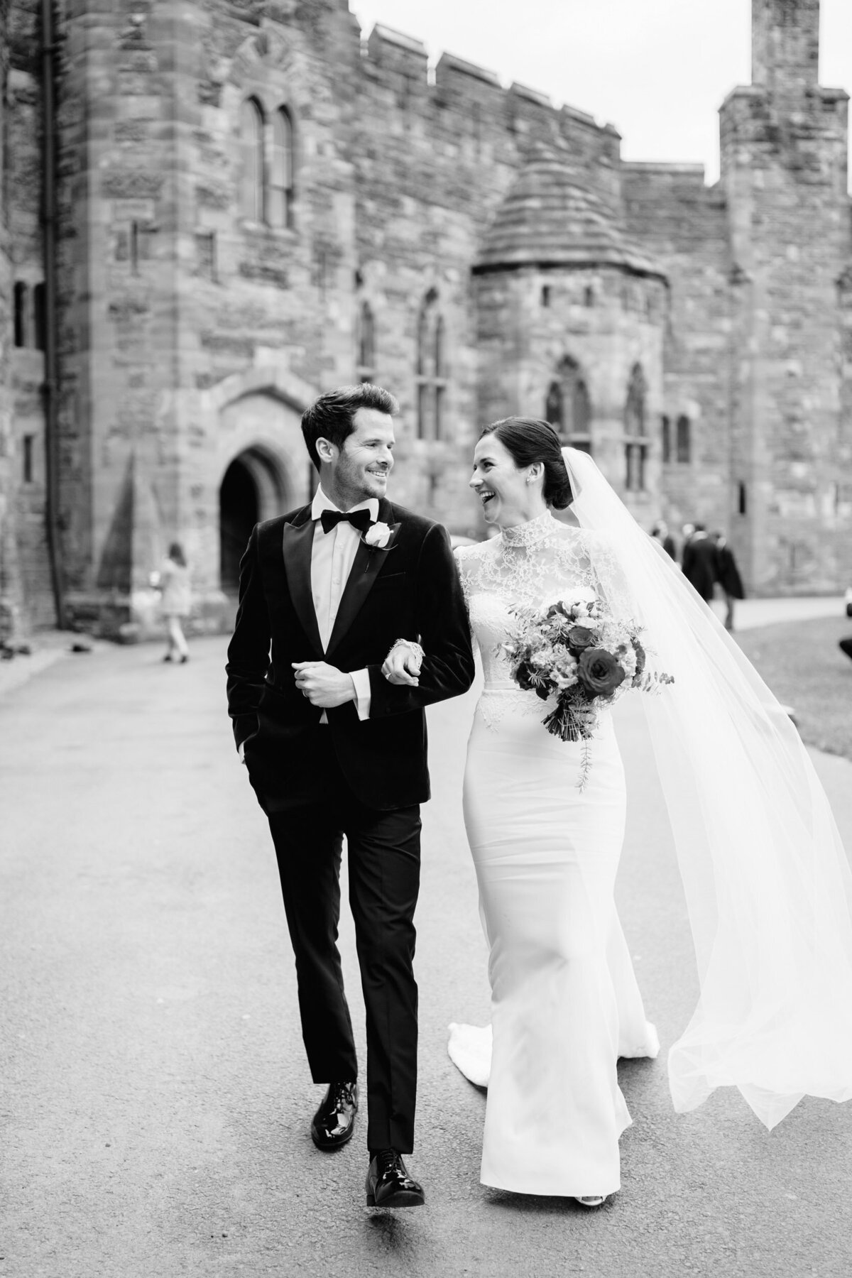 bride and groom walking with peckforton castle in the background