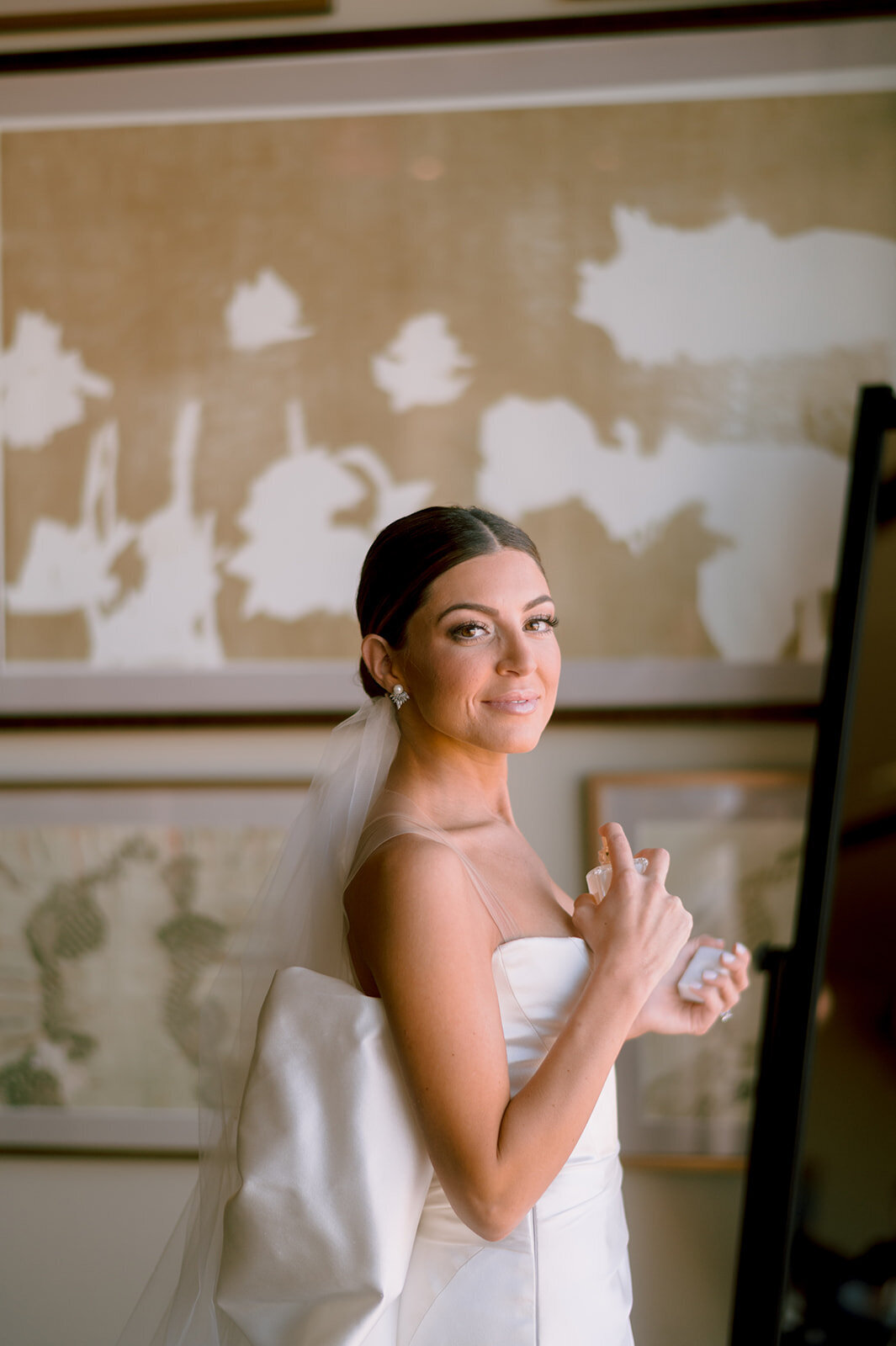 bride sprays herself with perfume in wedding attire prior to her new haven lawn club wedding photo by cait fletcher photography