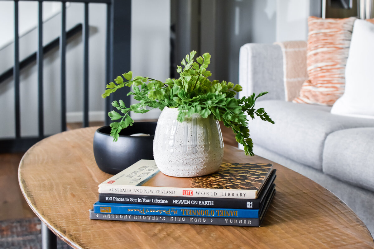 A potted plant sits on a stack of books next to a candle on a wood coffee table