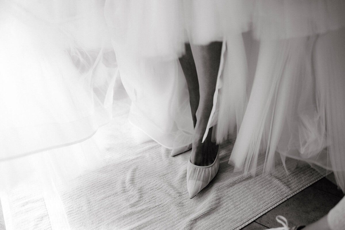 Black and white, close-up shot of the bride's shoes while she's wearing it, at The Ausable Club, New York.