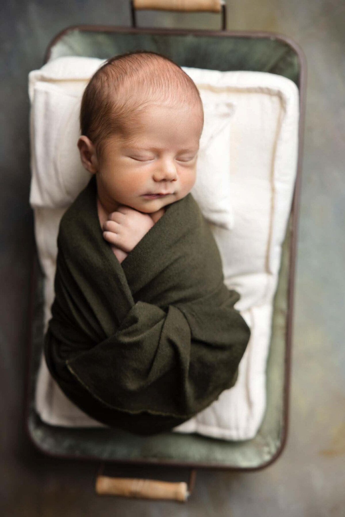 newborn baby wrapped in green fabric sleeping on a small mattress in a metal prop