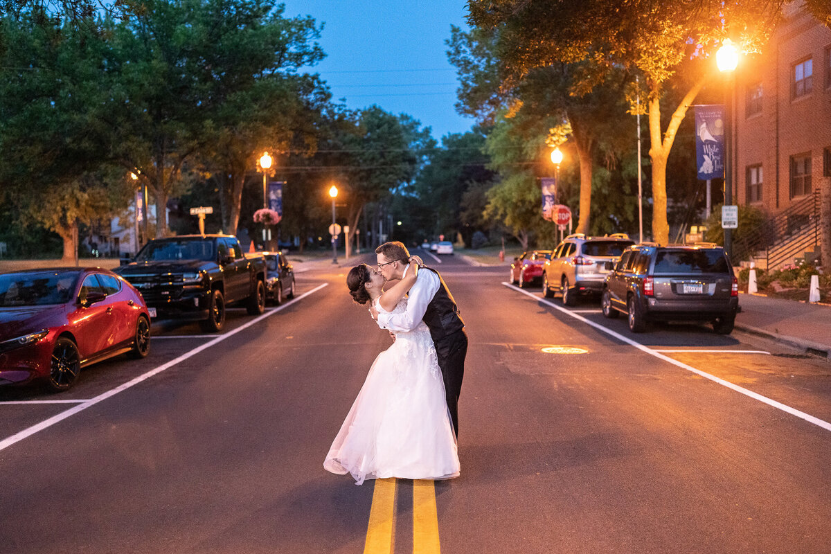Bride and groom kiss in the middle of the street at night.