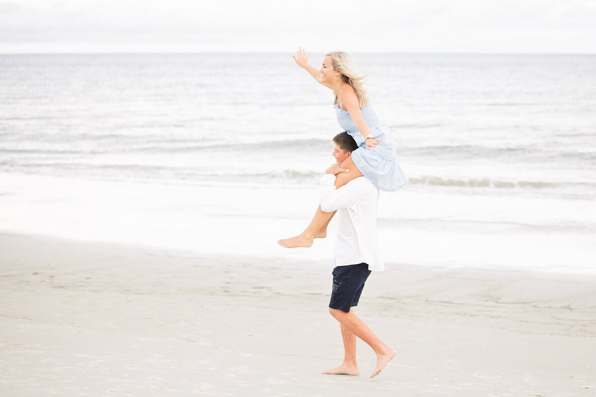 Girl is on boyfriends shoulder walking on the beach