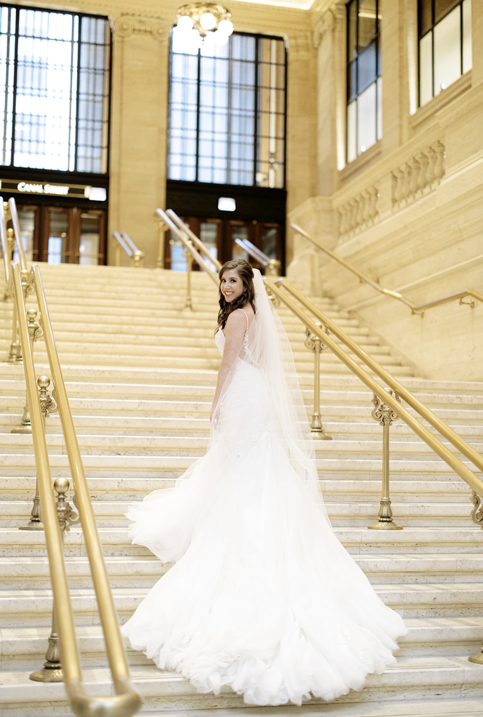 Chicago bride with brown hair and veil looks over her shoulder while standing on steps as gown cascades.
