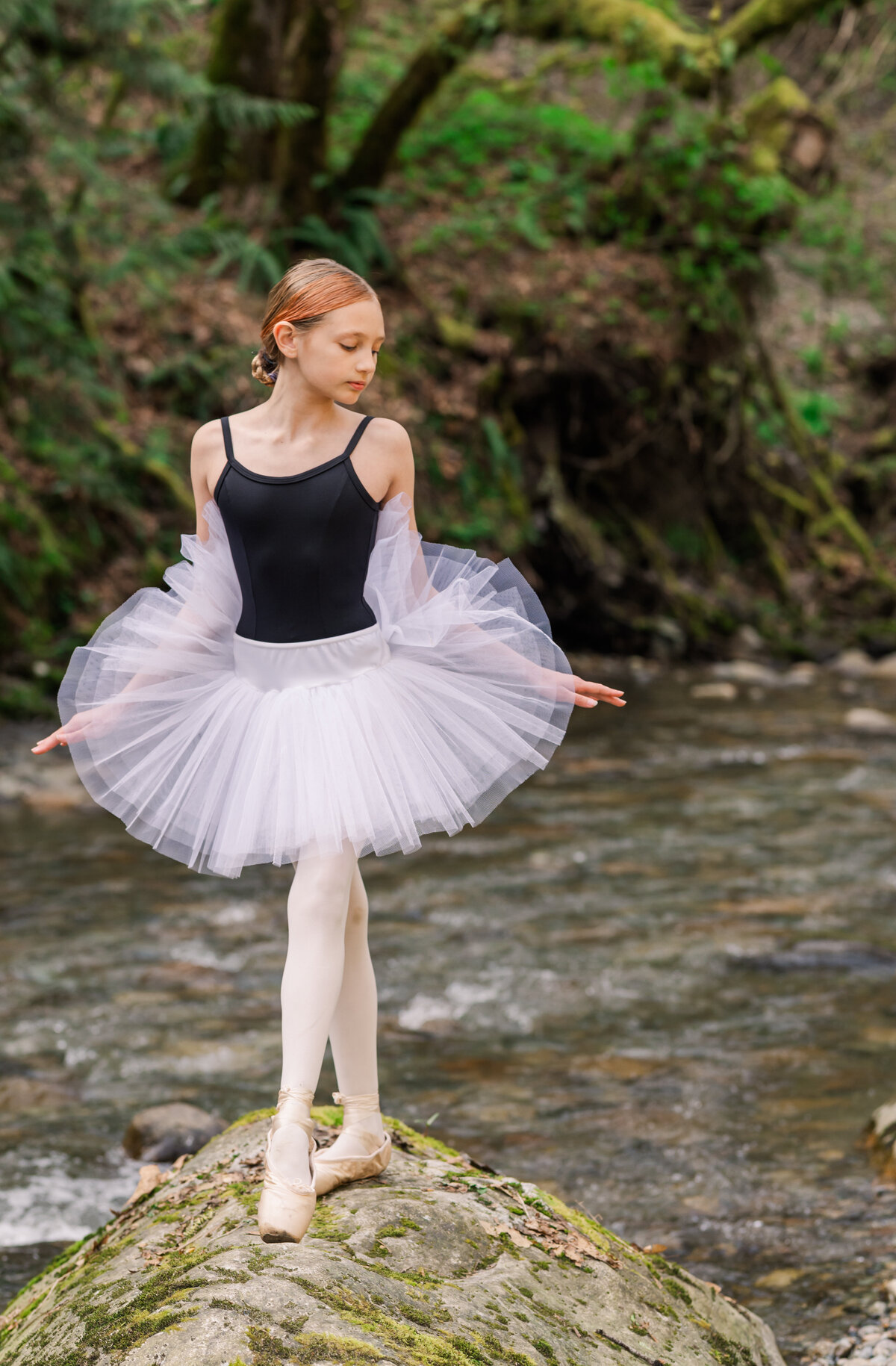 Young ballet girl in pointe shoes with black & white costume. She stands on a rock hands to the side and face to right side.