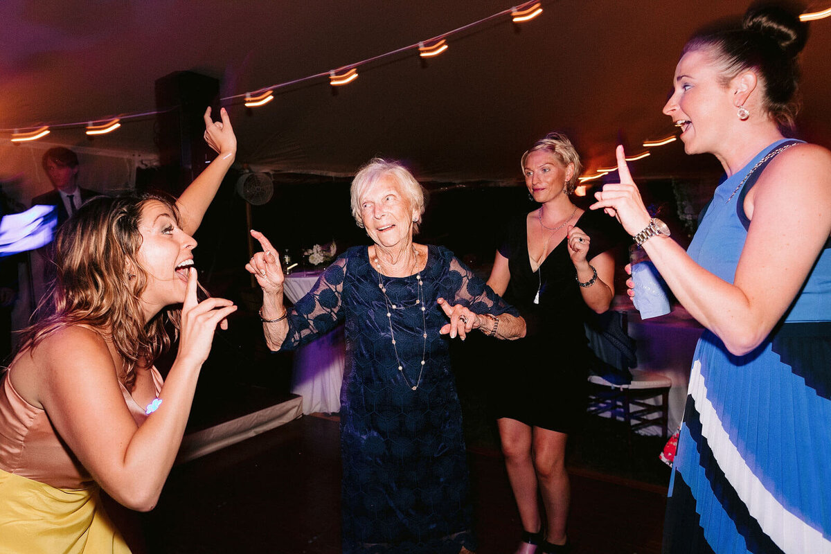 An old woman and three younger ones are dancing at a wedding reception in Cape Cod Summer Tent, Osterville, MA.