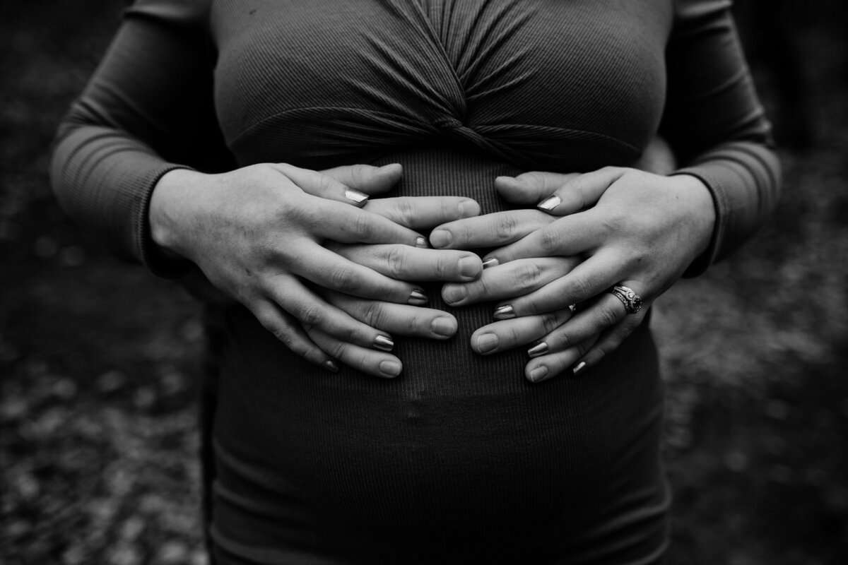 blank and white maternity photo of husband and wife's hands on pregnant belly