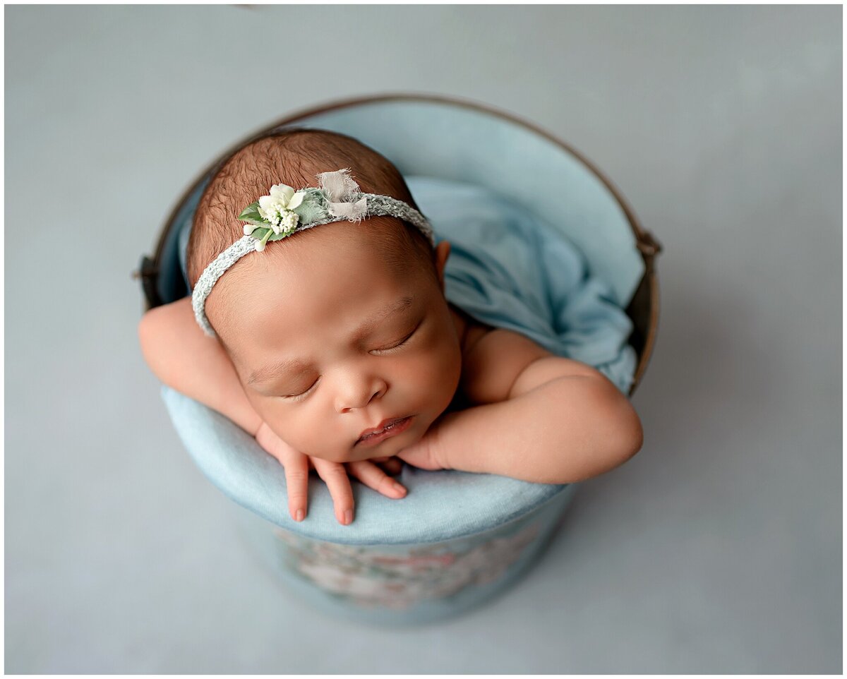 newborn girl in baby blue headband and in bucket