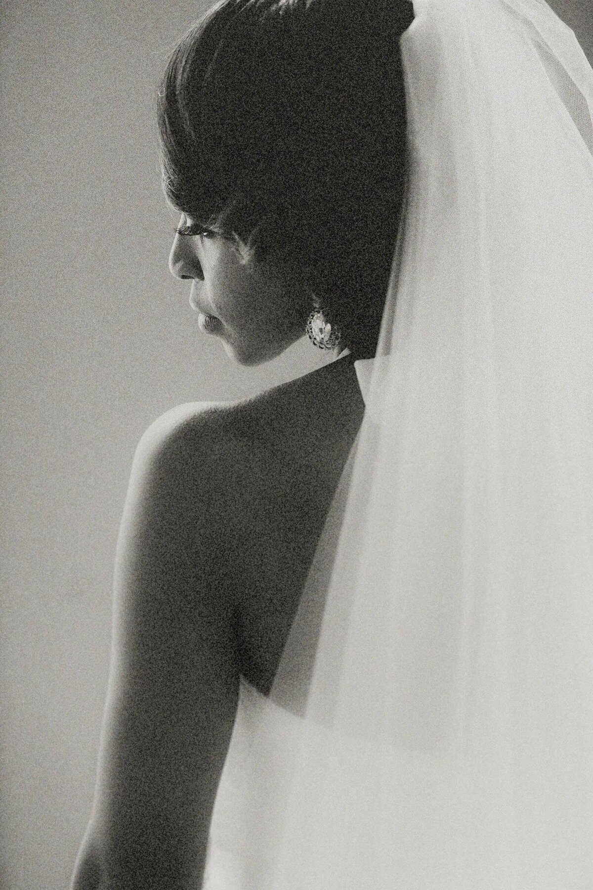 A side profile of a bride in a classic updo, her delicate veil and elegant earrings