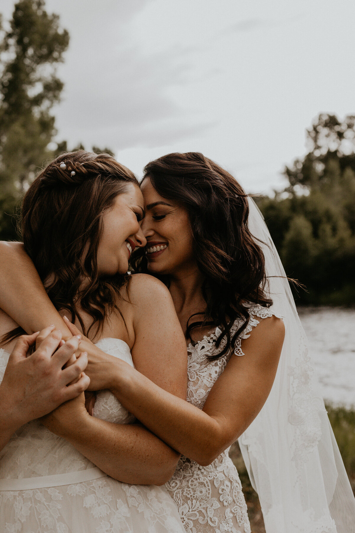 same sex couple holding each other and smiling in front of a river