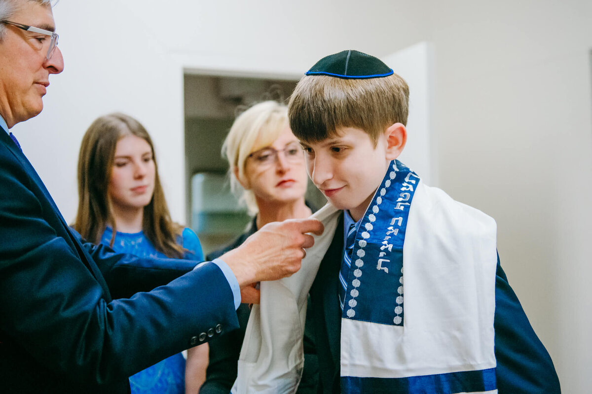 A rabbi adjusts a boy's tallit while preparing for his bar mitzvah
