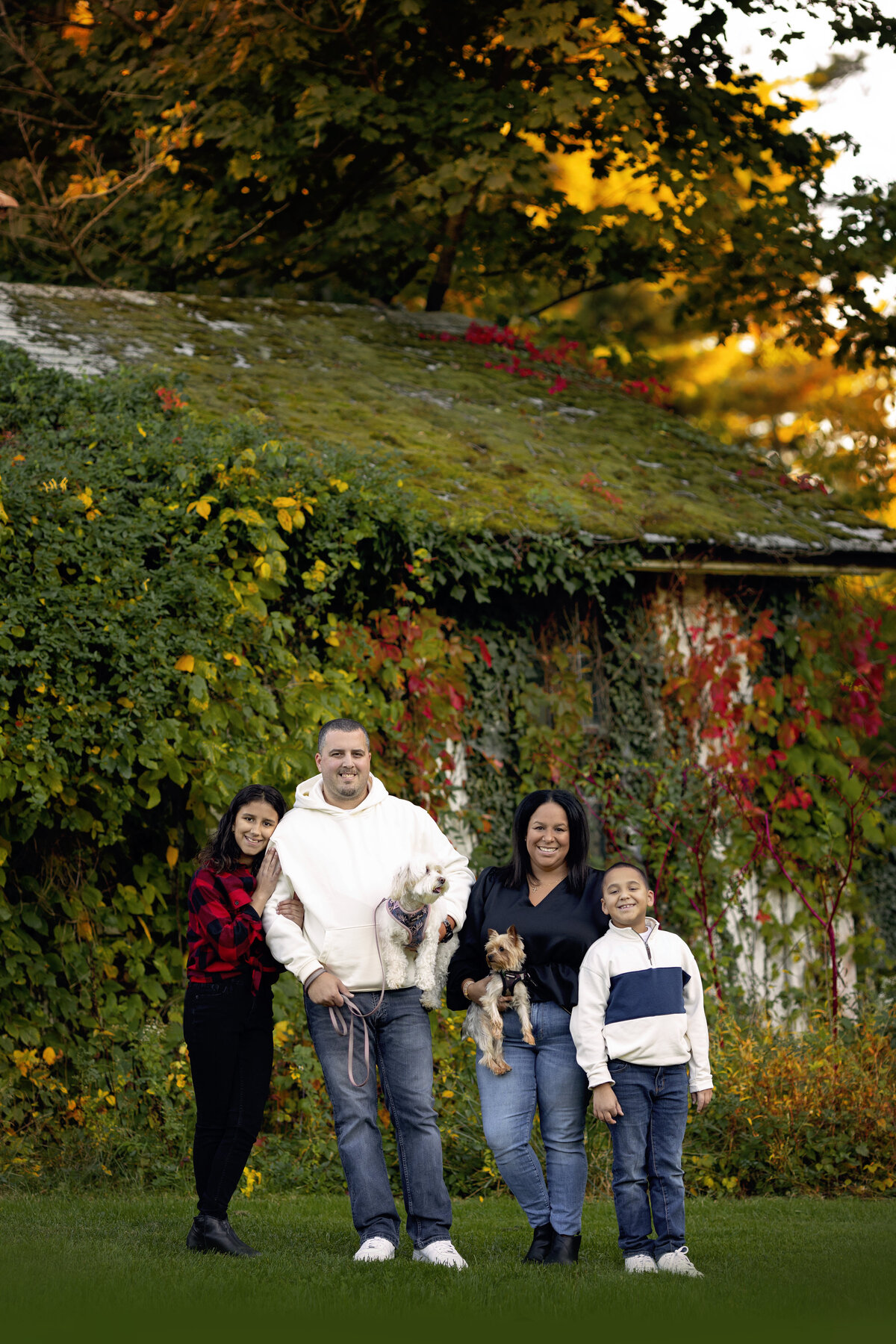 A mom and dad stand by a vine covered structure holding two tiny dogs with their teen daughter and son at their sides taken by a New Jersey Family Photographer