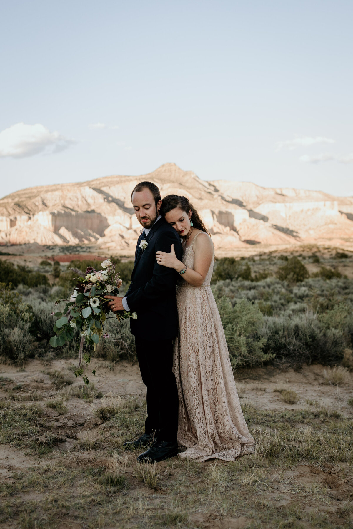 bride hugging groom from behind in front of a red rock mountain