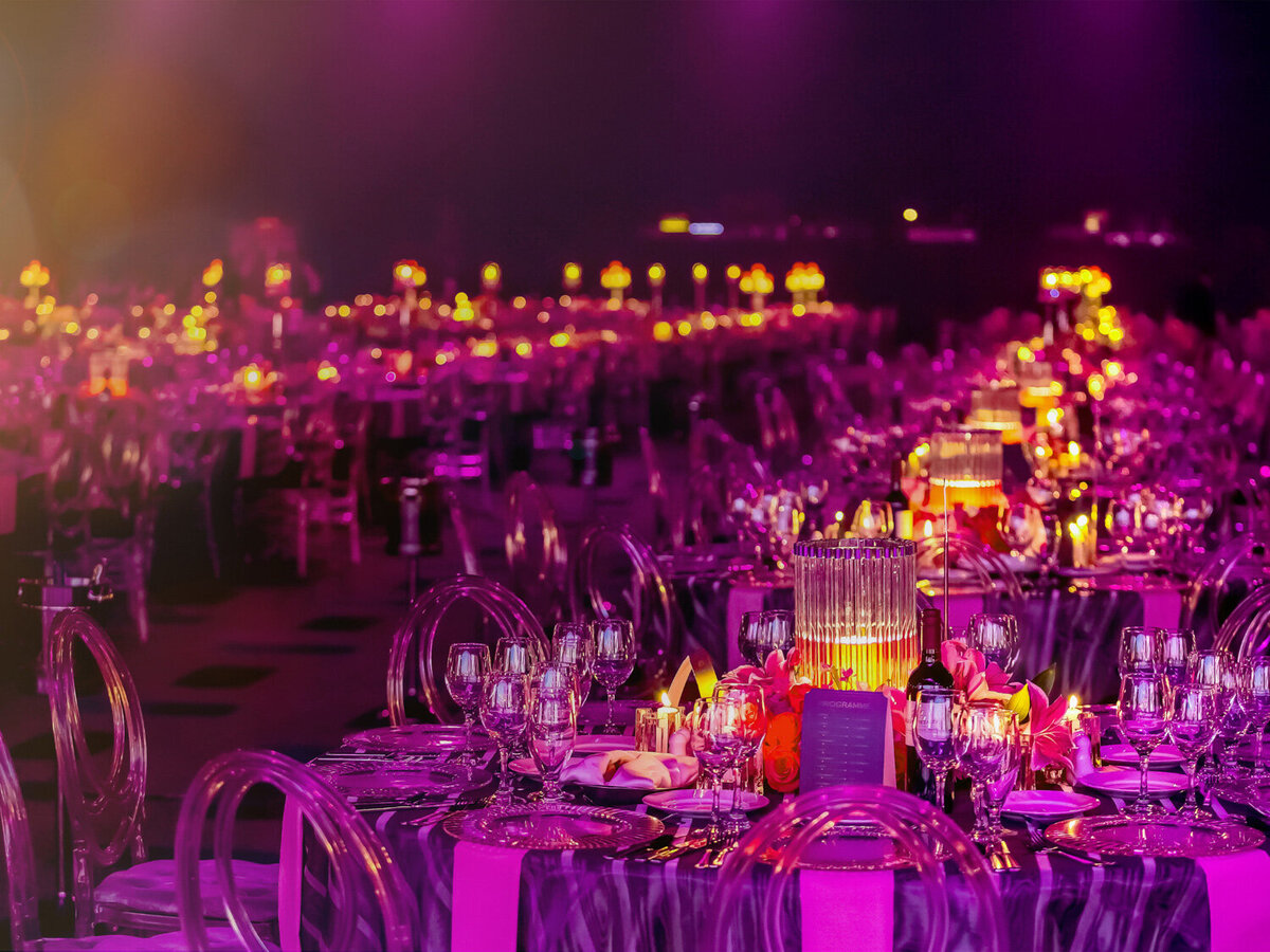 A lot of tables and chairs with lighted candles and purple lights