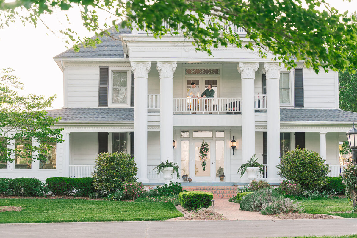 A same sex couple standing on the balcony of Highrock Farms at sunset in the spring by Raleigh wedding photographer, JoLynn Photography