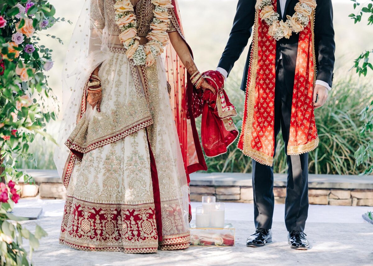 A bride and groom in traditional indian wedding attire holding hands during a ceremony.
