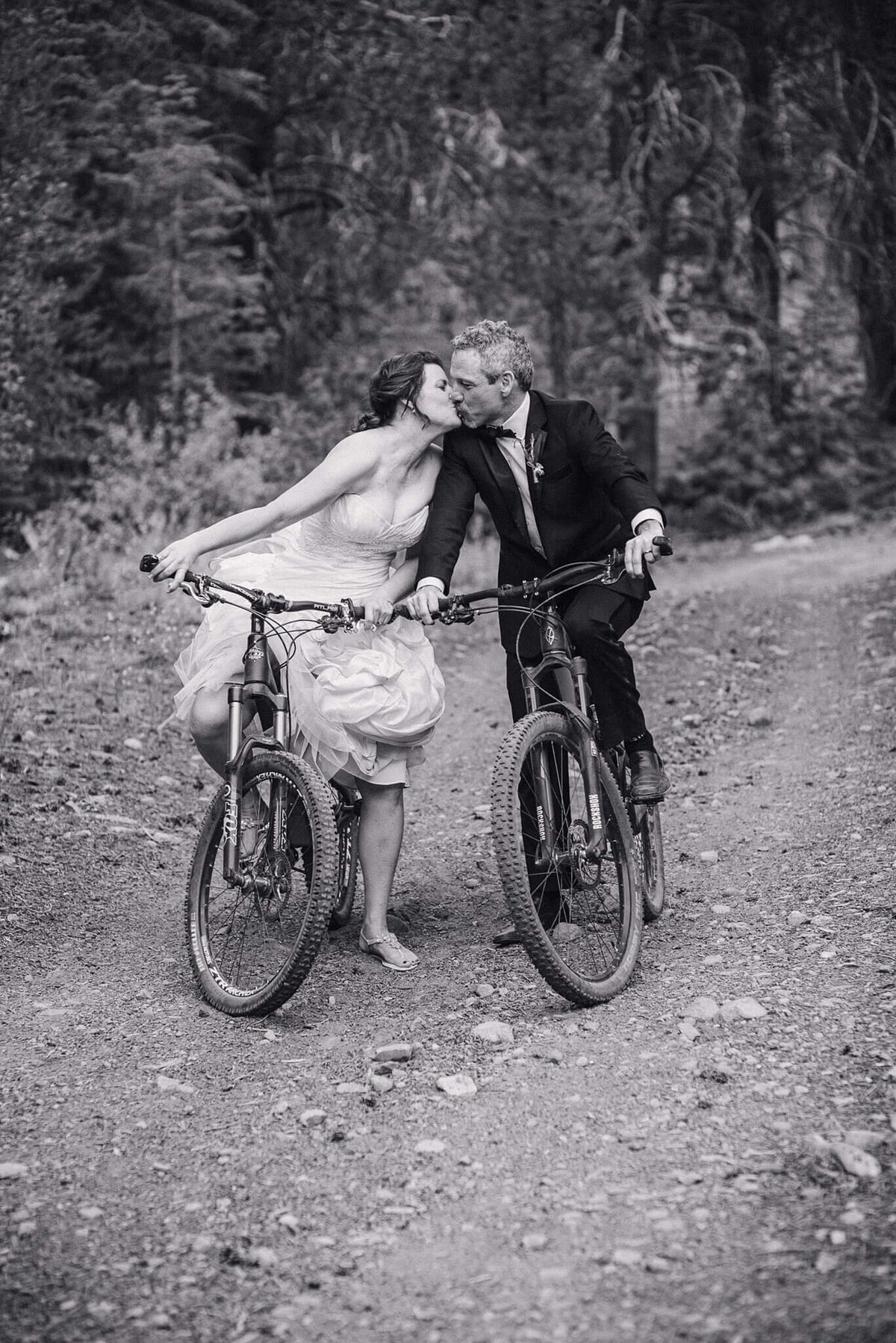 bride and groom on mountain bikes kissing , black and white image
