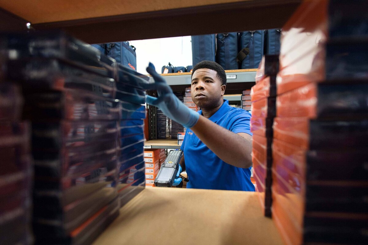 A man uses a scanner to check inventory of a product in a warehouse. Creative warehouse shot taken through the shelving