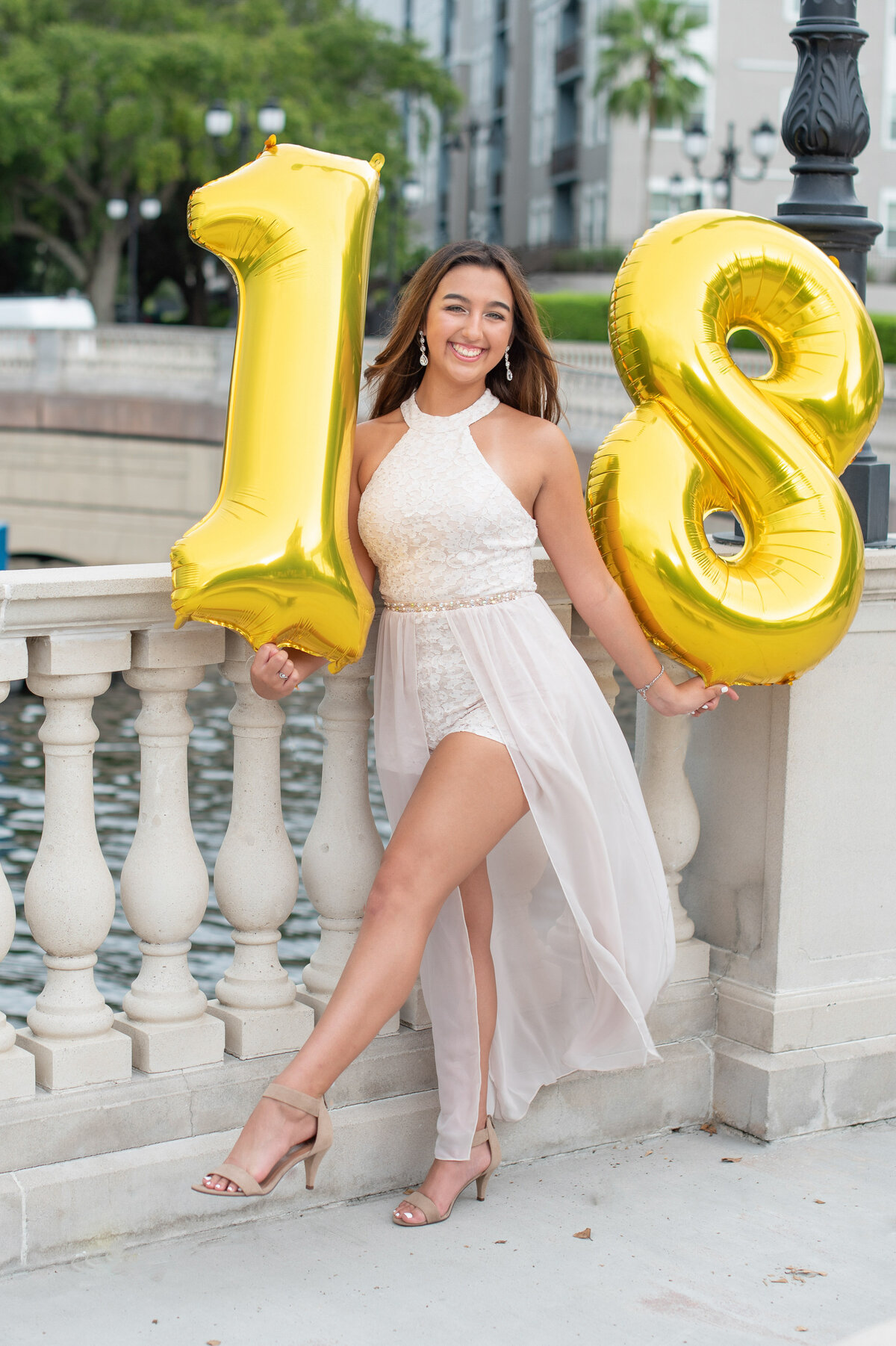 High school senior girl holding gold "18" balloons posing with leg kicked out.