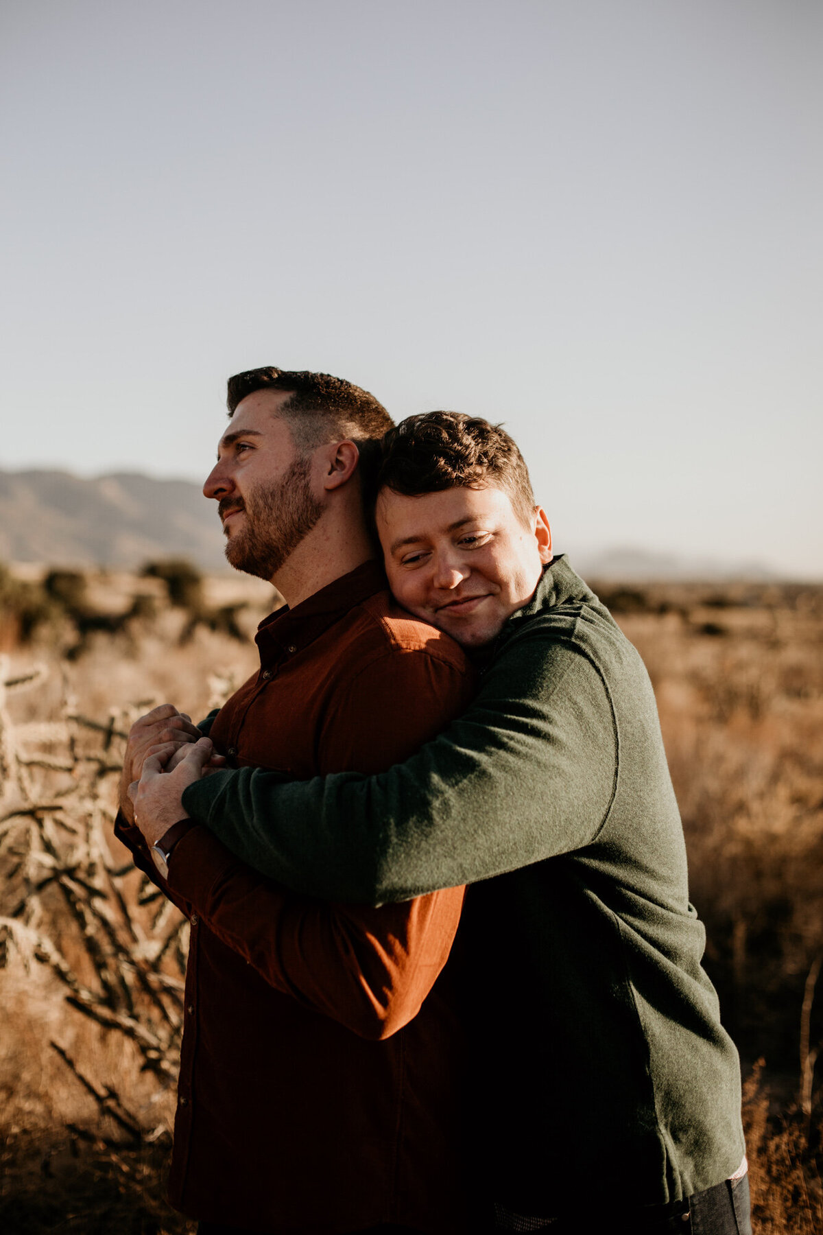 man hugging same sex fiancé from behind and smiling