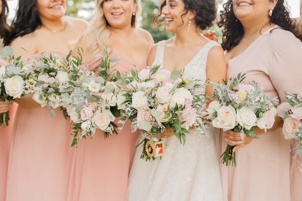 Bride and bridesmaids in pastel dresses holding floral bouquets at a wedding in Davenport, focusing on the bouquets with a gentle smile.