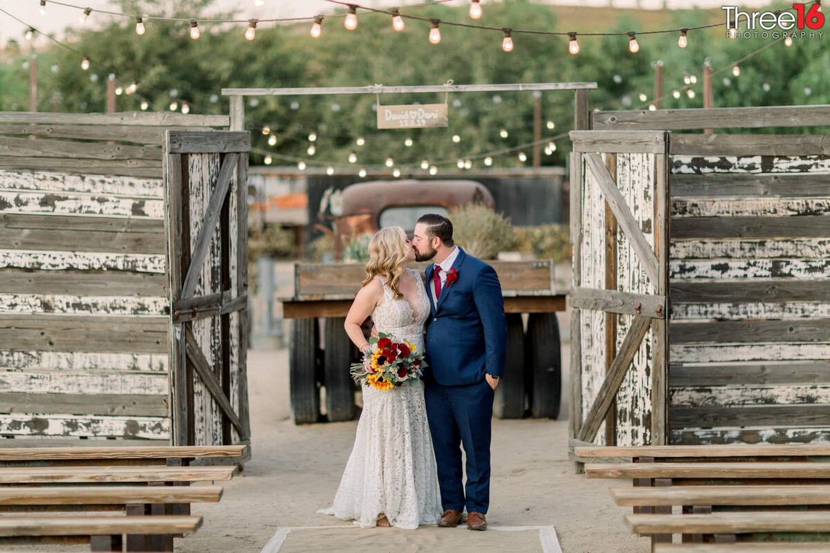 Bride and Groom stand in a rustic doorway and share a sweet kiss