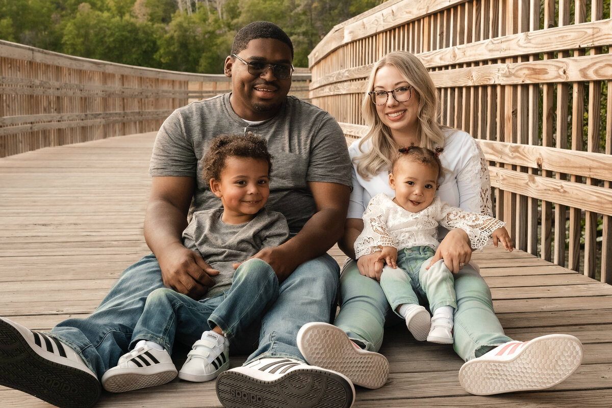 Family smiles with kids on a bridge.