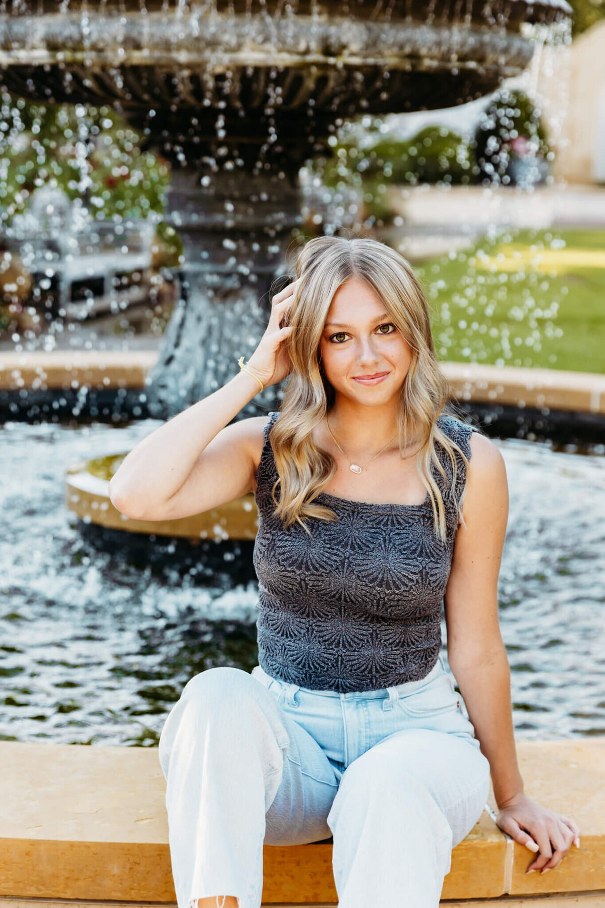 glamorous teen girl in a grey top and light blue jeans playing with her hair and staring confidently into the camera for her Green Bay Senior photo session