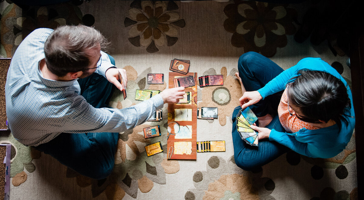 Overhead view of a couple sitting on the ground playing a card game.