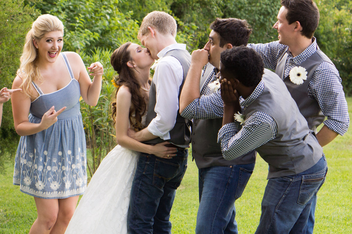 Bride & Groom kissing with bridal party snickering