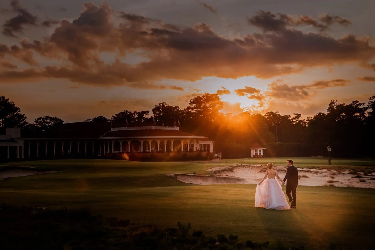 The golden hour sun casts a warm glow on a bride and groom walking hand in hand across a golf course