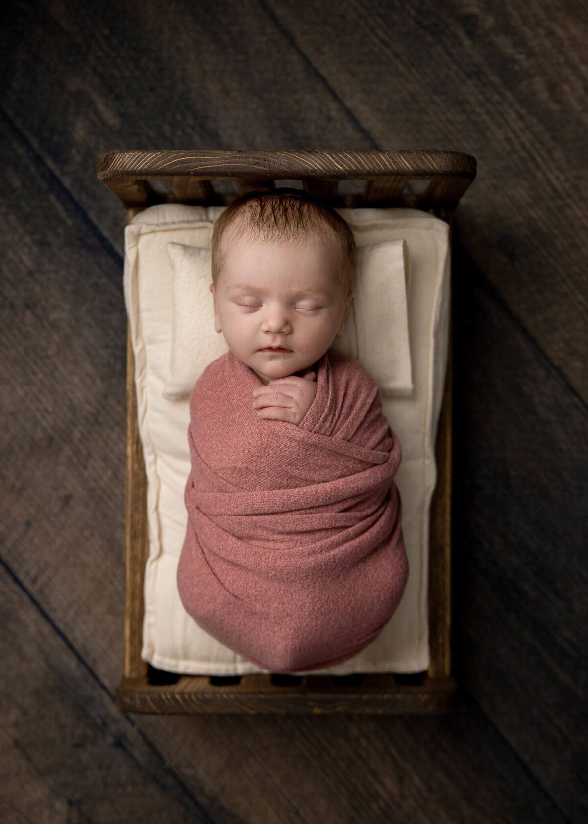 newborn baby wrapped in  a pink fabric asleep in a tiny wooden bed