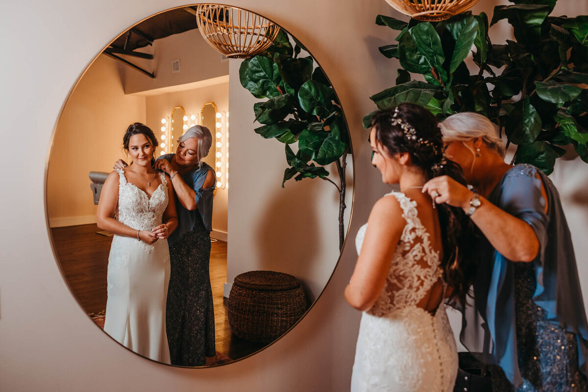 Photo of a bride getting her wedding dress on while her mom helps and admires her in the mirror