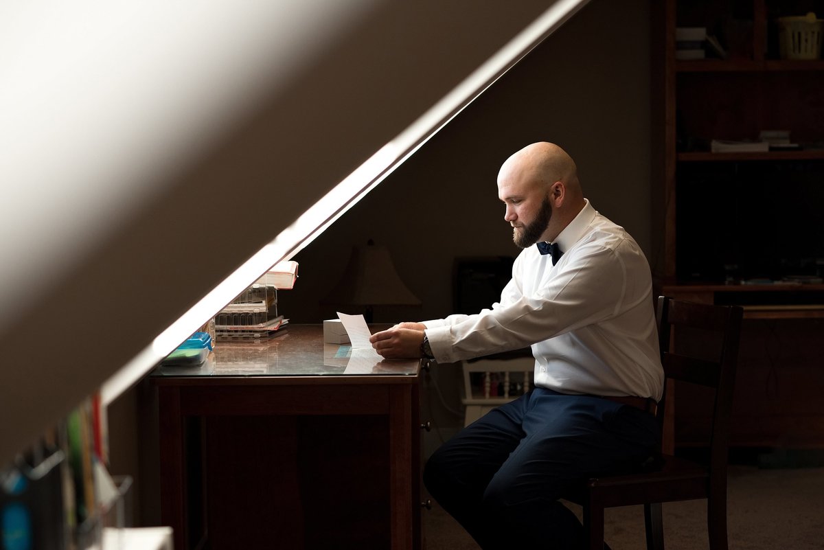 Groom sitting at an antique desk writing a letter to his fiance before they elope