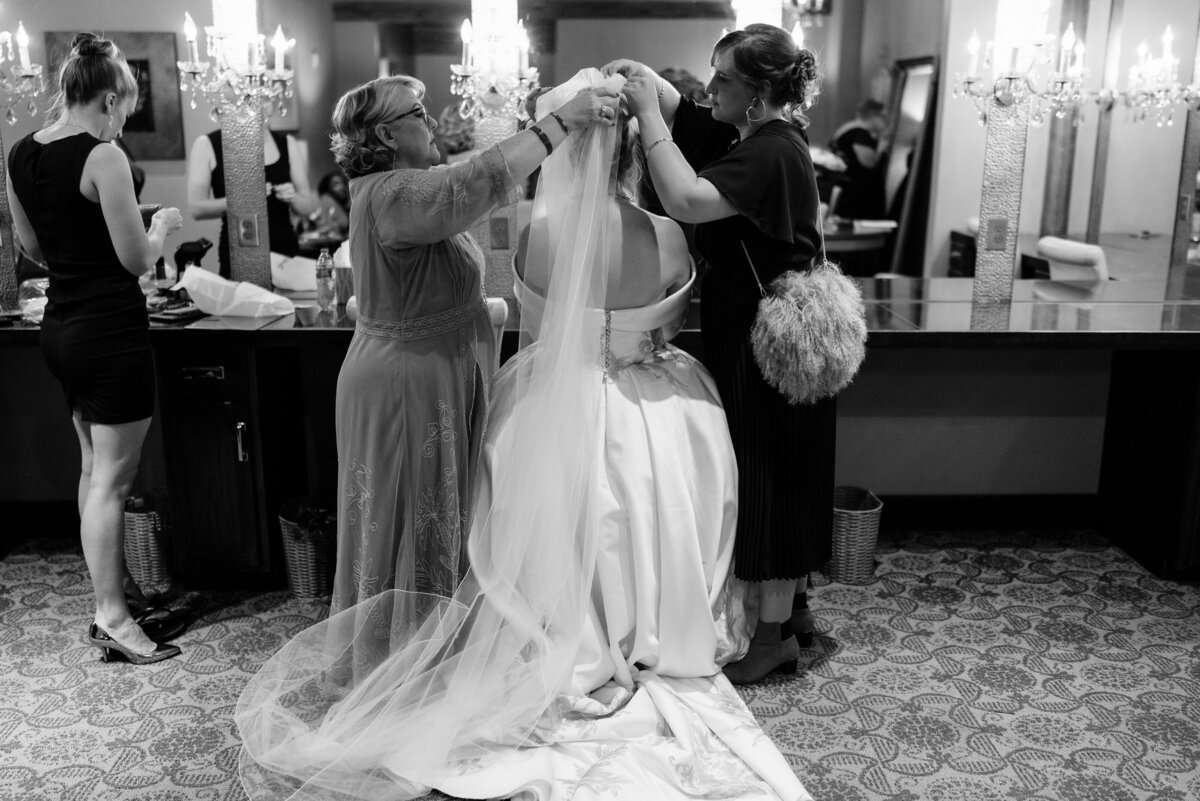 Mom help bride put her veil in while she sits in front of a vanity.