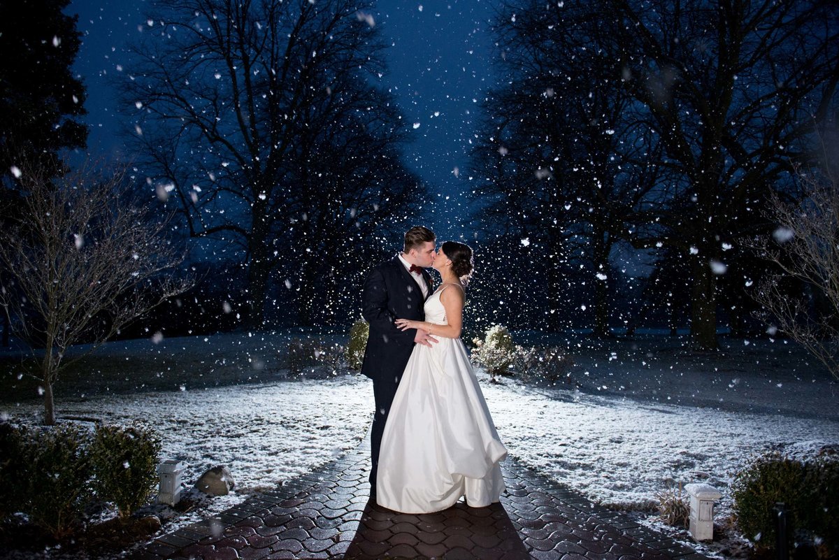 Bride and groom kissing outside during a snow shower at The Mansion at Oyster Bay