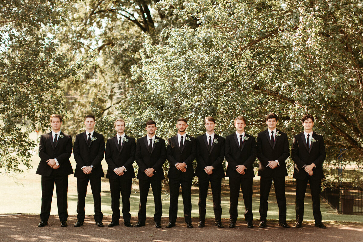 Groom with his eight groomsmen in black suits and ties standing side by side